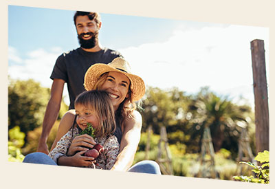 Image of a family on a farm with a father standing, and mother sitting with daughter in her lap holding some vegetables