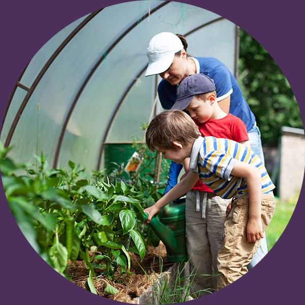 Image of a woman with two young children in a greenhouse garden looking at plants