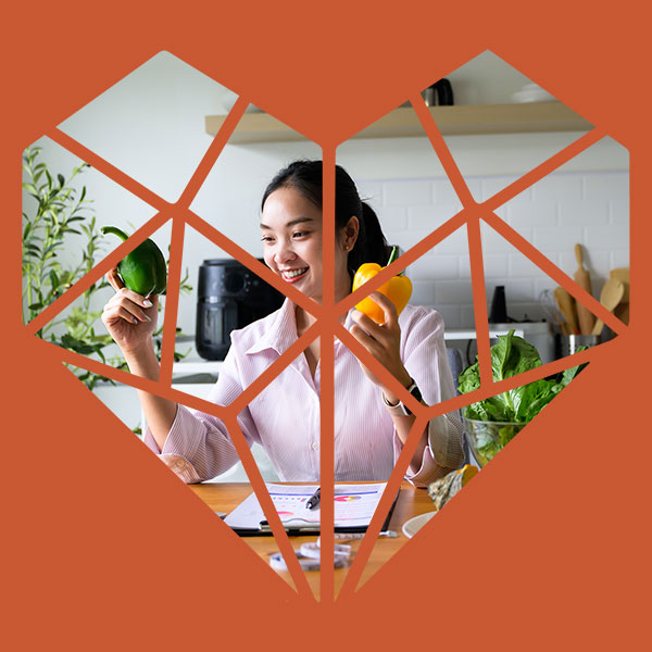 A smiling woman in a kitchen holding up fresh bell peppers