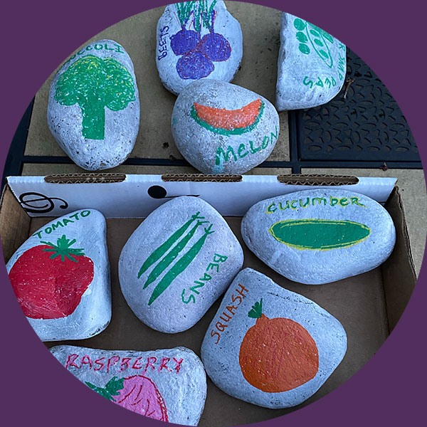 Rocks in a crate that are painted with fruits and veggies on them